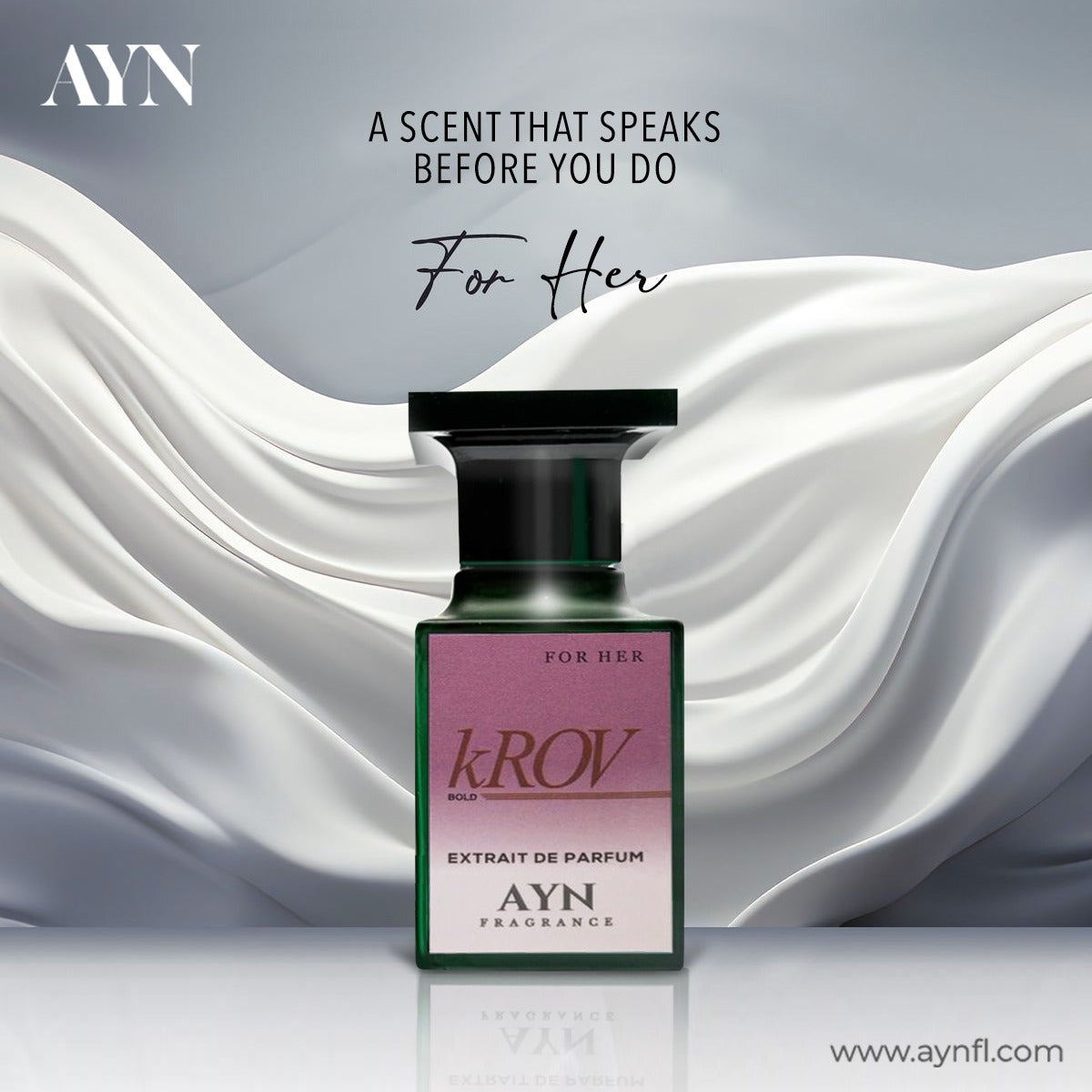 A bottle of AYN For Her Extrait de Parfum centered against a draped white satin background with gray gradient edges. The bottle is dark green glass with a black cap and a pink-to-white label featuring the kROV logo.